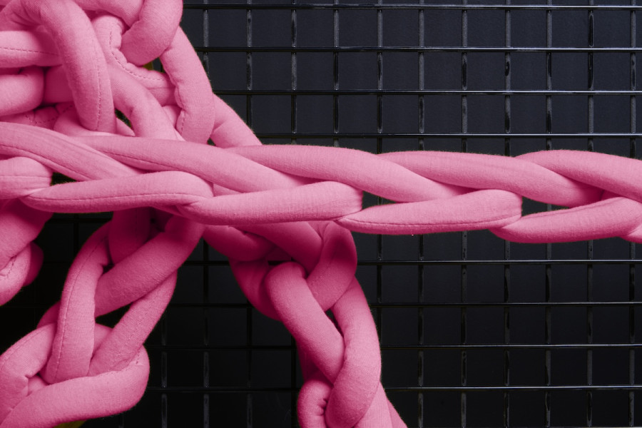 Candy pink stuffed textile chains stretch against a black metal grid background.