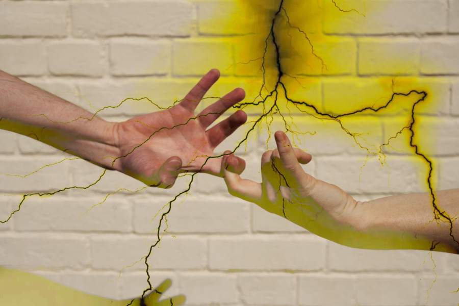 Two hands are linked by their pointer fingers in front of white brick. A yellow lightening effect is overlayed atop the image